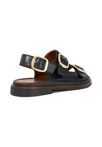 Black leather sandals featuring two large gold buckles, open design, brown insole, and a flat rubber sole with a textured edge.