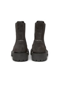 Bottes de cheville en suede noir avec une semelle en caoutchouc épaisse, des panneaux latéraux élastiques et une marque sur le talon, présentant une texture lisse et un design minimaliste.
