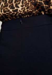 Pantalons taille haute noirs en tissu lisse et texturé. Fermeture éclair notable avec un tirant rond au niveau de la taille.