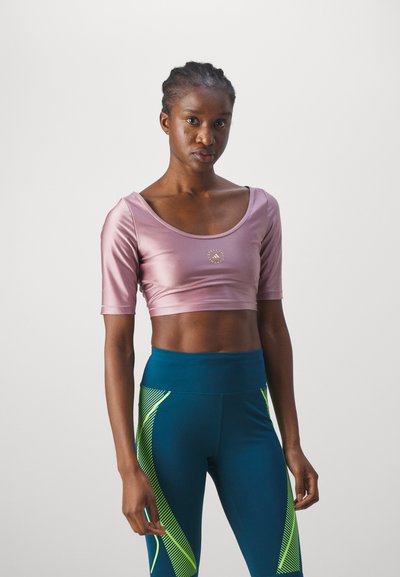 Kortermet, rosa satin crop-top med rund hals og gulllogo, kombinert med blå leggings med neongrønne diagonale striper.
