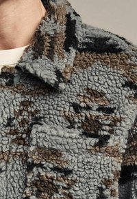 Fleecejacke mit einem strukturierten Muster in Grau, Schwarz und Braun, mit Stehkragen und einer Detailtasche vorne.