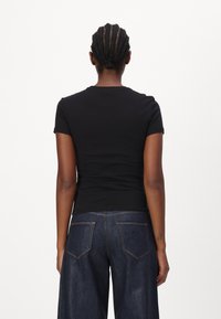 Černé tričko s krátkým rukávem a kulatým výstřihem, přiléhavý střih, spárované s tmavě modrými denimovými kalhotami s širokými nohavicemi a zadními kapsami.