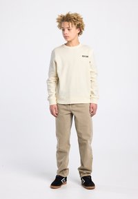 Sweat-shirt crème avec texte « NEW YORK », pantalon khaki coupe droite, et baskets noires. Texture lisse et décontractée.