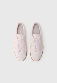 Gaiši pelēkas zamšādas kedas ar persiku toņiem akcentiem un trim svītrām sānos. Aprīkotas ar gumijas zoli un auklu aizdari.