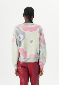Felpa grigia lavorata a maglia con motivi floreali oversize in rosa, grigio e verde. Presenta un colletto e polsini a coste, abbinata a pantaloni in pelle rossa.
