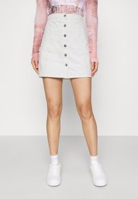 Valkoinen farkkuhame, jossa on A-linjainen siluetti, etupainonappi kiinnitys, viisi metallinappia ja ompelusyksityiskohtia. Yhdistetty valkoisten tennareiden ja sukkien kanssa.