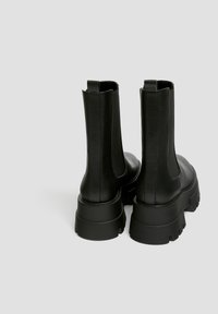 Stivali alla caviglia in pelle nera con finitura testurizzata, pannelli laterali elasticizzati e suole in gomma spesse e robuste. Tacco elevato per un'altezza aggiuntiva.