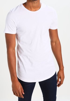 T-shirt blanc à col rond en tissu doux, à manches courtes et ourlet arrondi. Porté avec un jean bleu foncé, mettant en valeur une silhouette ajustée.