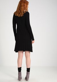 Svart ribbad klänning med långa ärmar, knälång. Har en utsvängd nederkant och textur. Parat med grå ankelboots och svarta strumpor.