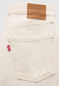 Πίσω τσέπη από κρεμ τζιν Levi's με κόκκινη ετικέτα Levi's στο πλάι και καφέ δερμάτινη ετικέτα Levi Strauss & Co. πάνω από τη μέση.