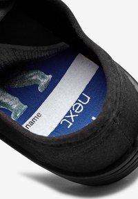 Schwarzes Leinenschuhinterior mit einer blauen Einlegesohle, die ein Grafikdesign und weiße Markenbeschriftung zeigt. Verfügt über eine glatte Textur und eine gepolsterte Fütterung.