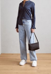 Chemise bleu marine à boutons avec poignets à volants, associée à un jean large bleu clair et des baskets blanches à plateforme ; tenant un petit sac noir.