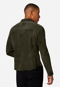 Olivgrön mockajacka med rak skärning, knäppta ärmslut och en subtil textur. Har en baketikett och rena sömmar.