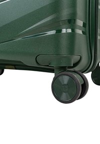 Esquina de equipaje rígido verde con ruedas spinner negras dobles y líneas de diseño horizontales elegantes en la superficie.