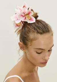 Accessorio per capelli con fiori in tessuto rosa e bianco, acconciato in un chignon. Lo sfondo è neutro, mettendo in risalto il design floreale.