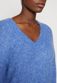 Närbild av en person som bär en fluffig blå V-ringad tröja, som visar en strukturerad stickad tyg och en silverfärgad hoop-örhänge.