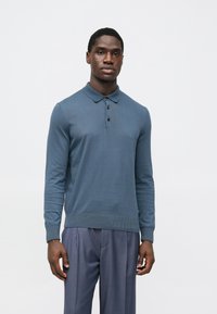 Polo azul de manga comprida feito de algodão macio. Apresenta gola com colarinho, carcela com três botões e punhos e bainha canelados.