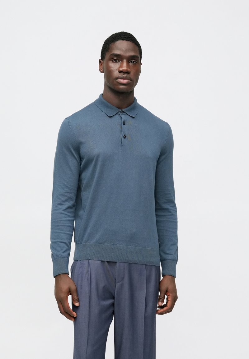 Polo azul de manga comprida feito de algodão macio. Apresenta gola com colarinho, carcela com três botões e punhos e bainha canelados.