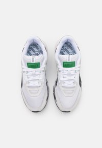 Chaussures de sport blanches avec une tige en maille, des accents noirs et un logo vert. Dotées de lacets, d'un col rembourré et de semelles intérieures à motifs.