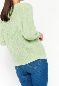 Pull en maille vert clair à la coupe décontractée, arborant un motif texturé et un ourlet côtelé, associé à un jean fitted bleu foncé.