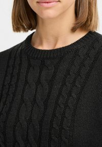 Svart stickad tröja med ett strukturerat kabelmönster, rund halsringning och ribbade muddar, som visar upp olika sticktekniker.