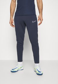 Mørkeblå joggers lavet af blødt stof, med en slank pasform, elastisk talje og et hvidt Nike-logo på venstre lår.