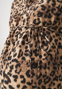 Tissu en imprimé léopard avec un fond beige et des taches noires. Il possède une ceinture à la taille pour un ajustement et une texture lisse et douce.