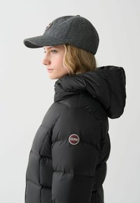 Schwarze Pufferjacke mit Kapuze, mit einem gesteppten Design und einem runden Logo-Patch. Graue Wollmütze mit gebogenem Schirm.