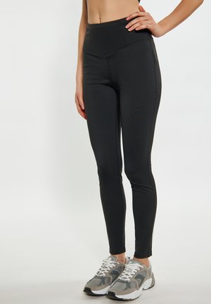 Schwarze hoch taillierte Leggings mit glatter Textur, dehnbarem Stoff und flachen Nähten. Kombiniert mit grauen und weißen Sportschuhen.