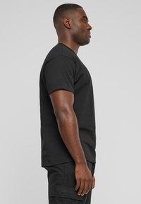 Sort kortærmet t-shirt lavet af bomuld, med rund hals og en afslappet pasform, vist på en mandlig model fra siden.