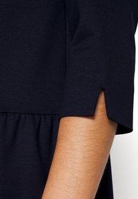 Marineblause mit kurzen Ärmeln, die eine Schlitzdetails am Bund aufweisen, aus einem glatten, elastischen Stoff und mit einem gerafften Taillenbund.