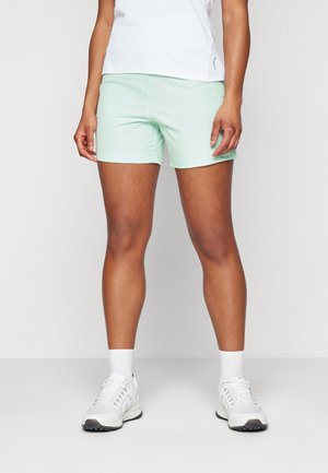 Shorts de sport vert menthe clair avec une texture lisse, présentant une coupe régulière et une taille élastique, associés à des chaussures de sport blanches.
