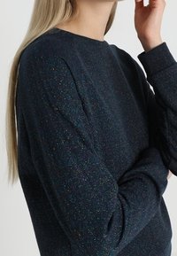 Marineblauwe sweatshirt met een subtiele glitterstructuur, voorzien van een ronde halslijn en lange mouwen. De stof zorgt voor een zachte, comfortabele uitstraling.