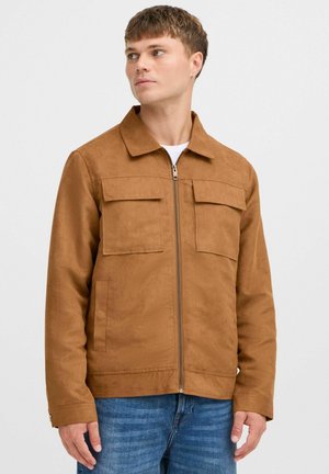 Brown suede jacket with a zip front, collared neck, and two chest pockets. The fabric has a soft texture and a clean, minimalist design.
