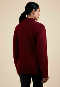Pulover tricotat de culoare burgundy, cu o croială lejeră, având tivuri și manșete cu model canalé, textură netedă și un design clasic al gulerului.