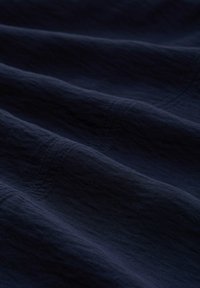 Tissu bleu marine au toucher doux, présentant de légères rides et des lignes de couture visibles. Matériau lisse et léger qui tombe en vague.