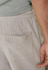 Hellgraue, wafflestrukturierte Sweatpants mit elastischem Bund und einer Seitentasche, teilweise sichtbar gegen ein grünes Oberteil.
