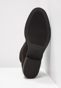 Bottines en daim noir avec un bout arrondi, une semelle en caoutchouc plate et un détail de texture antidérapant. Logo du fabricant imprimé sur la semelle.