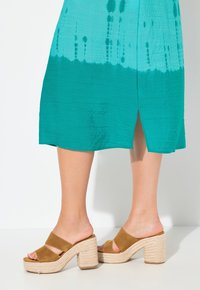 Braune Wildleder-Plateausandalen mit breiten Riemen und einer geflochtenen Jutessohle, kombiniert mit einem türkisfarbenen Kleid, das einen Farbverlauf und einen Seitenschlitz hat.