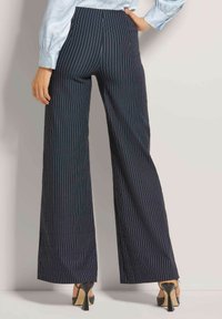Marineblauwe pinstriped wijde broek met een getailleerde pasvorm, met een soepele textuur en een hoge taille. G gedragen met zwarte stilettohakken.
