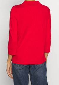 Roter Strickpullover mit Kragen, dreiviertellangen Ärmeln, gerippten Bündchen und einer lockeren Passform. Die Rückseite hat einen leicht längeren Saum.