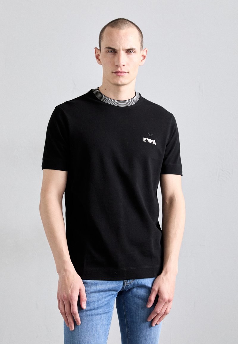 T-shirt noir à manches courtes avec un col rond, présentant un col rayé, un petit logo brodé sur la poitrine gauche et une coupe classique.