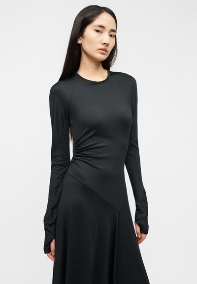 Μαύρο φόρεμα με μακριά μανίκια, διαθέτει εφαρμοστό μπούστο, πτυχώσεις στα πλαϊνά και αέρινη φούστα· κατασκευασμένο από λείο, ελαστικό ύφασμα.