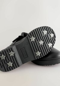 Zwarte instapschoenen met een getextureerd bovenwerk en rubberen zool, versierd met zilveren glinsterende sterrenpatronen aan de onderkant.