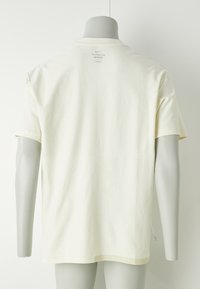Kreemi värvi Nike T-särk, mis on valmistatud pehmest kangast, omab ümarat kaelust, lühikesi varrukaid ja väikest sildi taga.