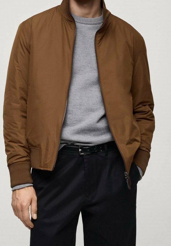 Veste aviateur marron avec col côtelé, fermeture éclair et poches latérales, portée sur un pull gris à col rond, associée à un pantalon foncé.