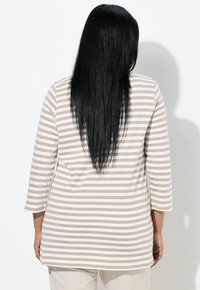 Beżowo-biały top w paski z długim rękawem i zaokrąglonym dołem. Miękki materiał o luźnym kroju, z widocznymi detalami przeszyć.