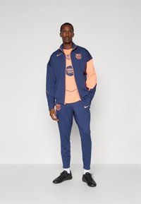 Navy sports tracksuit with coral accents, featuring a zip-up jacket and matching pants, made from breathable fabric. Embroidered team logo.
