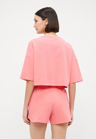 Cropped pink cotton t-shirt with short sleeves paired with matching pink shorts. Smooth texture, simple design, and relaxed fit.