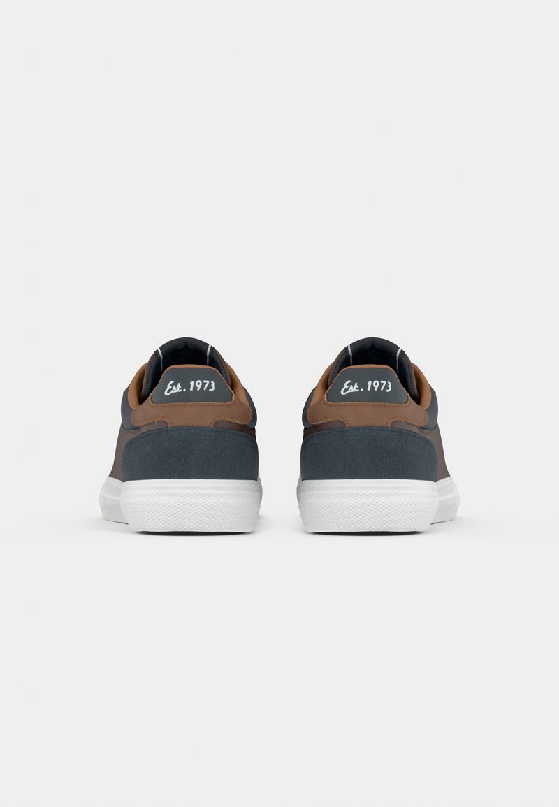 Zapatillas para hombre con parte superior en gris oscuro y acentos en ante marrón, suela de goma blanca, punta redonda y etiqueta "Est. 1973" en el talón.